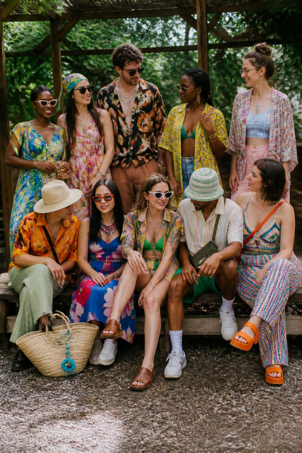 A group of people wearing colorful and layered summer outfits outdoors, standing and sitting casually with natural daylight and soft shadows.