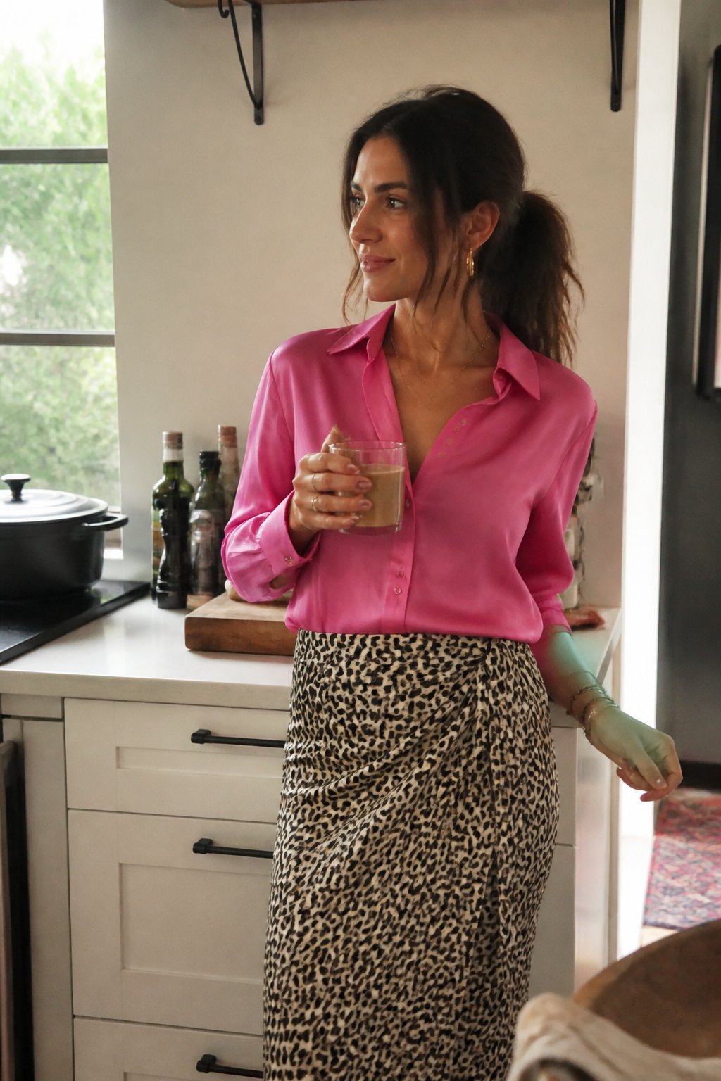A woman wearing an animal-print wrap skirt and hot-pink silk blouse in a softly lit casual setting with natural shadows and everyday objects around her.