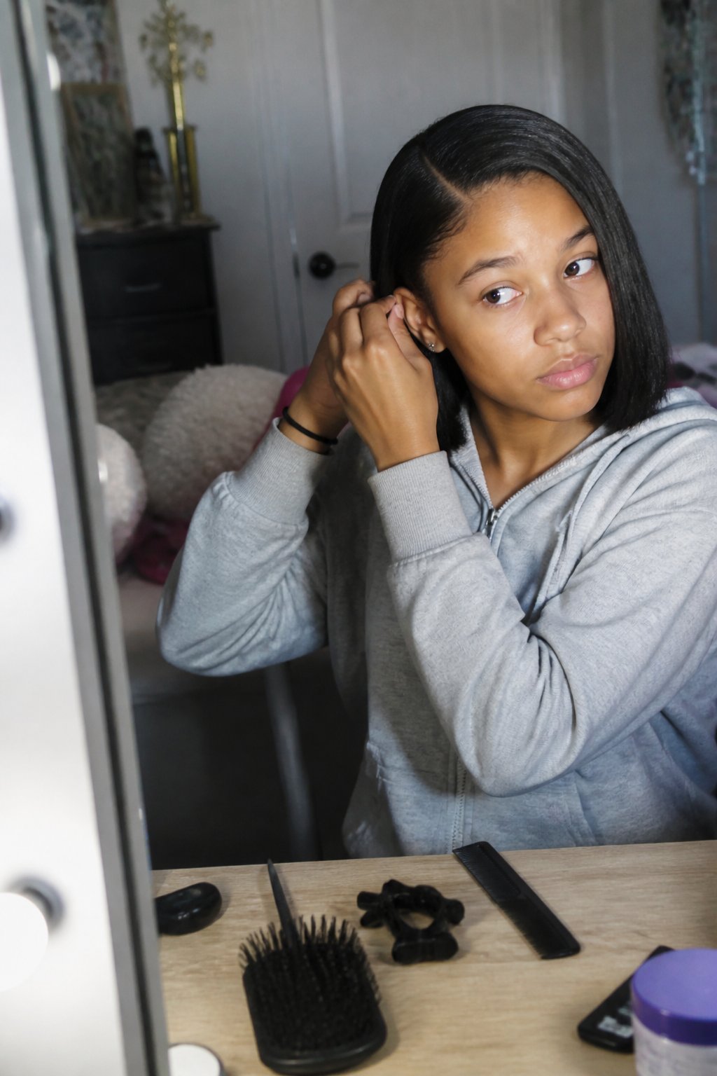 A person styling their sleek straight bob with a deep side part in a softly lit room, with hair tools and hands visible on a wooden surface.