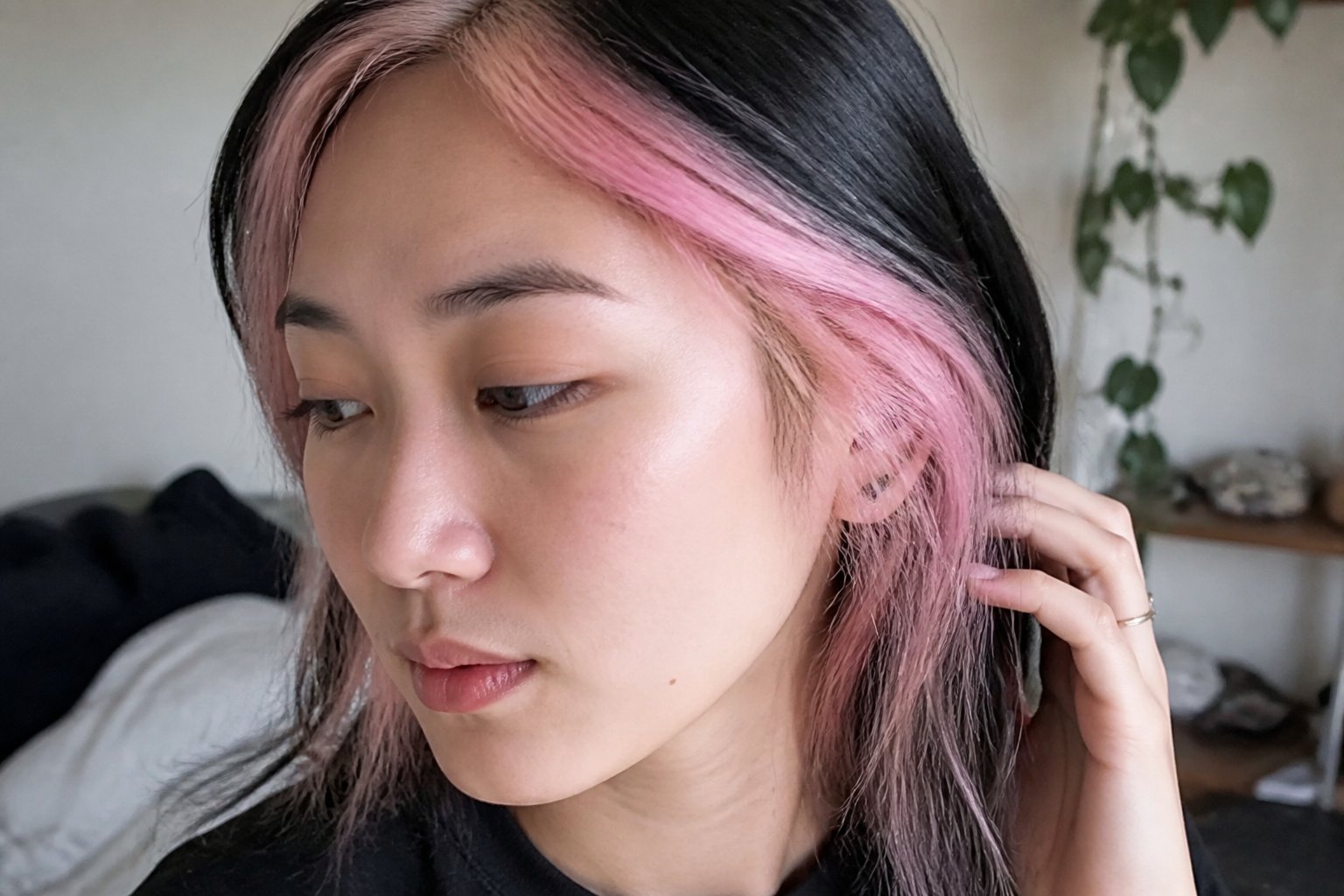 A person with pastel pink peekaboo skunk stripe hair in natural daylight, with hands and hair styling tools visible in a casual indoor setting.