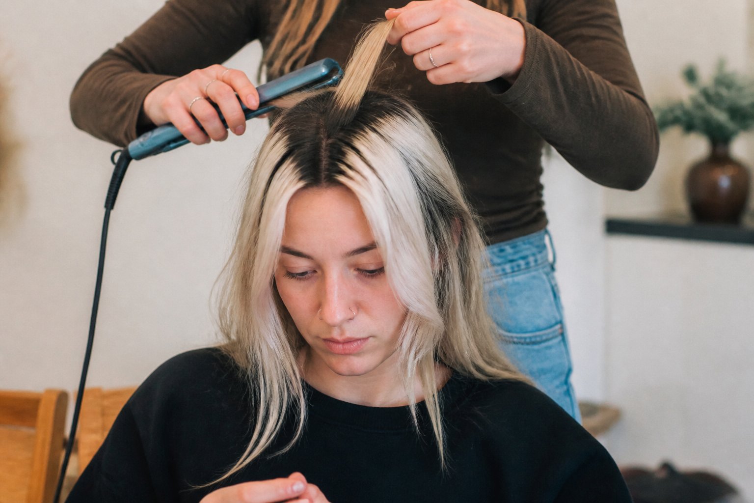 A person with reverse dark-rooted blonde skunk stripe hair is shown in a casual setting, with hands gently touching the hair and simple hair tools nearby.