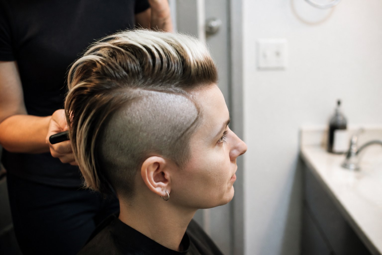 Person with a chunky buzzed-side skunk stripe hairstyle in soft daylight, with hair styling tools nearby.