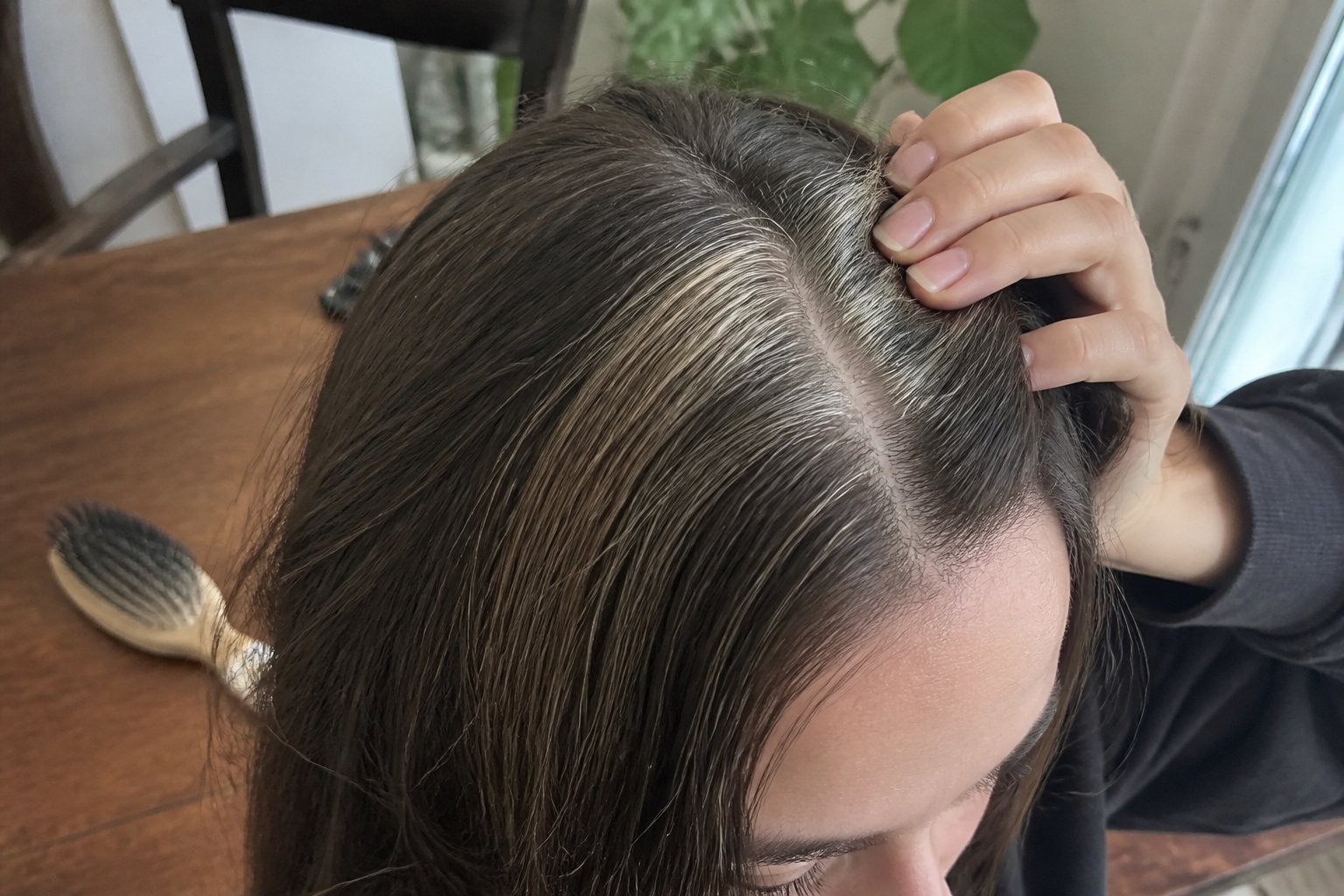 Close-up of a person with ash-brown baby stripe hair showing a skunk stripe pattern, with a hand gently touching the hair and everyday objects in the background.