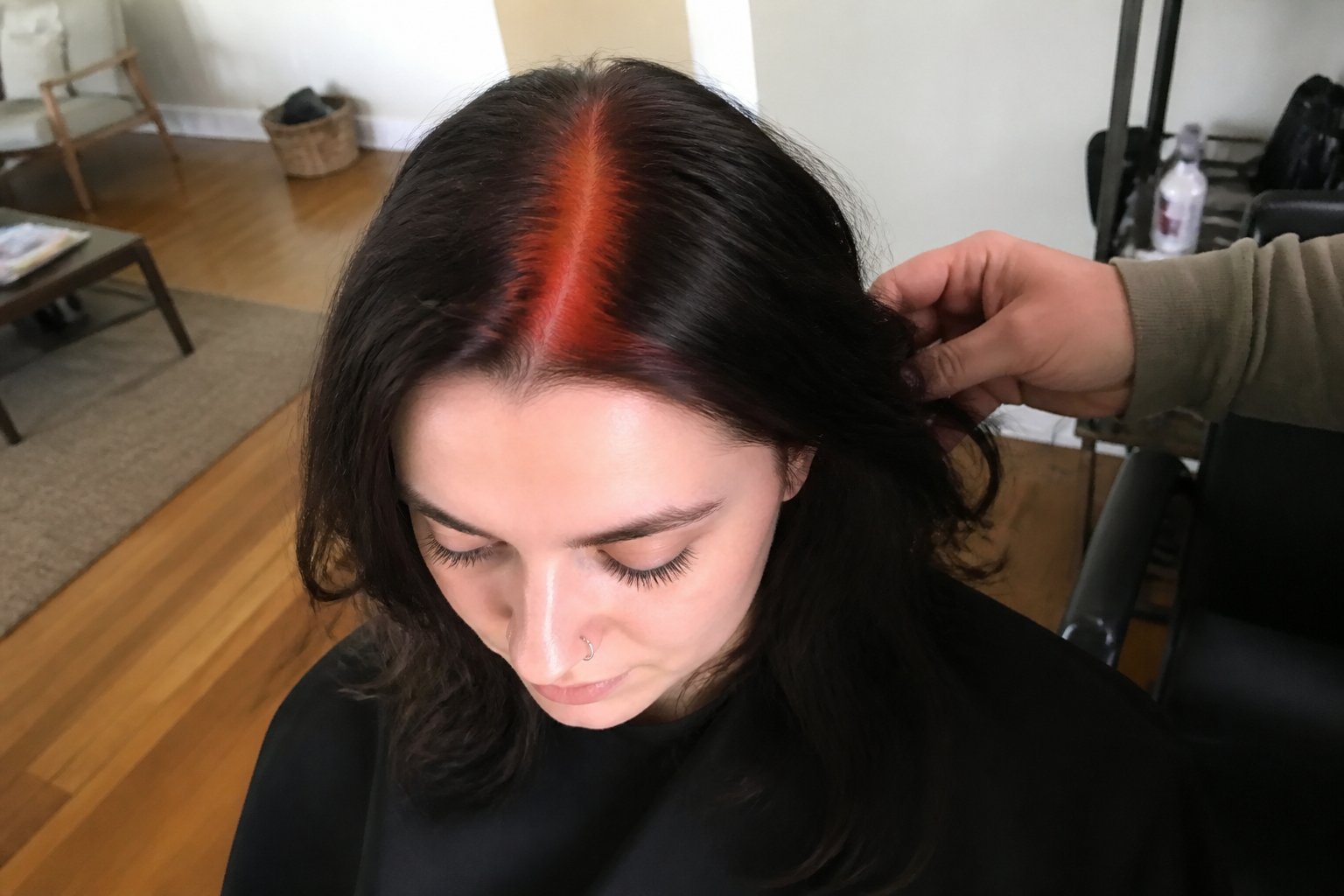 A person with a copper-red single front stripe in their hair, shown in a casual setting with natural daylight and everyday objects around.