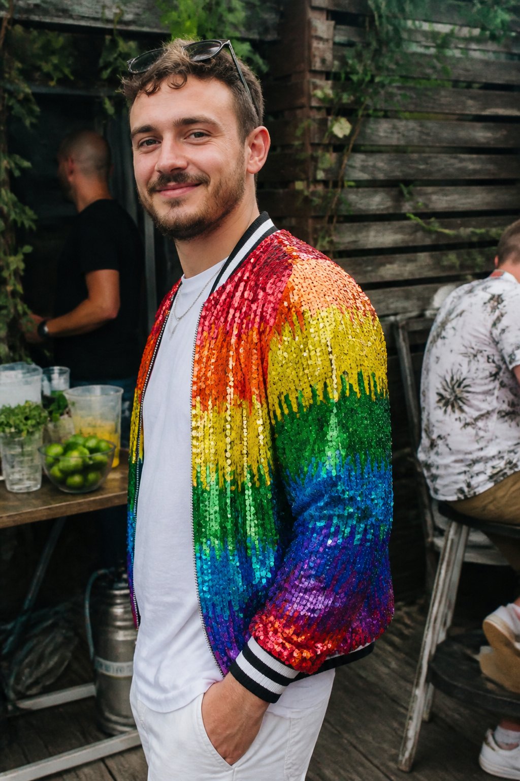 Person wearing a rainbow sequin bomber jacket outdoors with soft daylight and casual surroundings.
