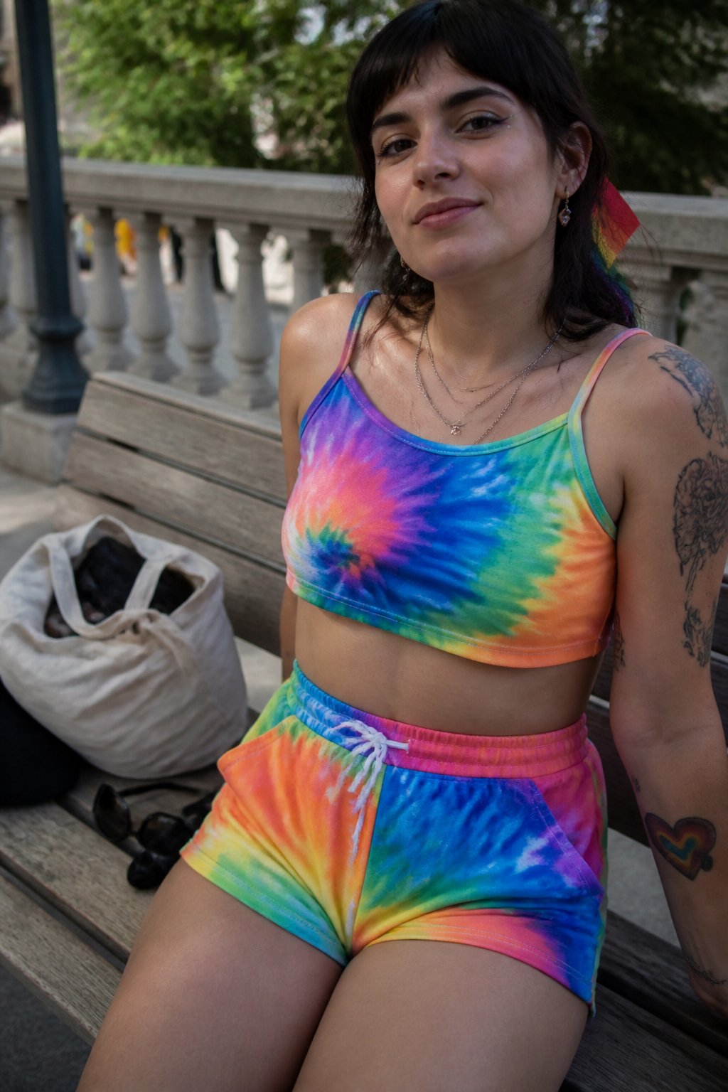 Person wearing a colorful tie-dye crop top and high-waist shorts outdoors in soft daylight, with casual objects nearby.