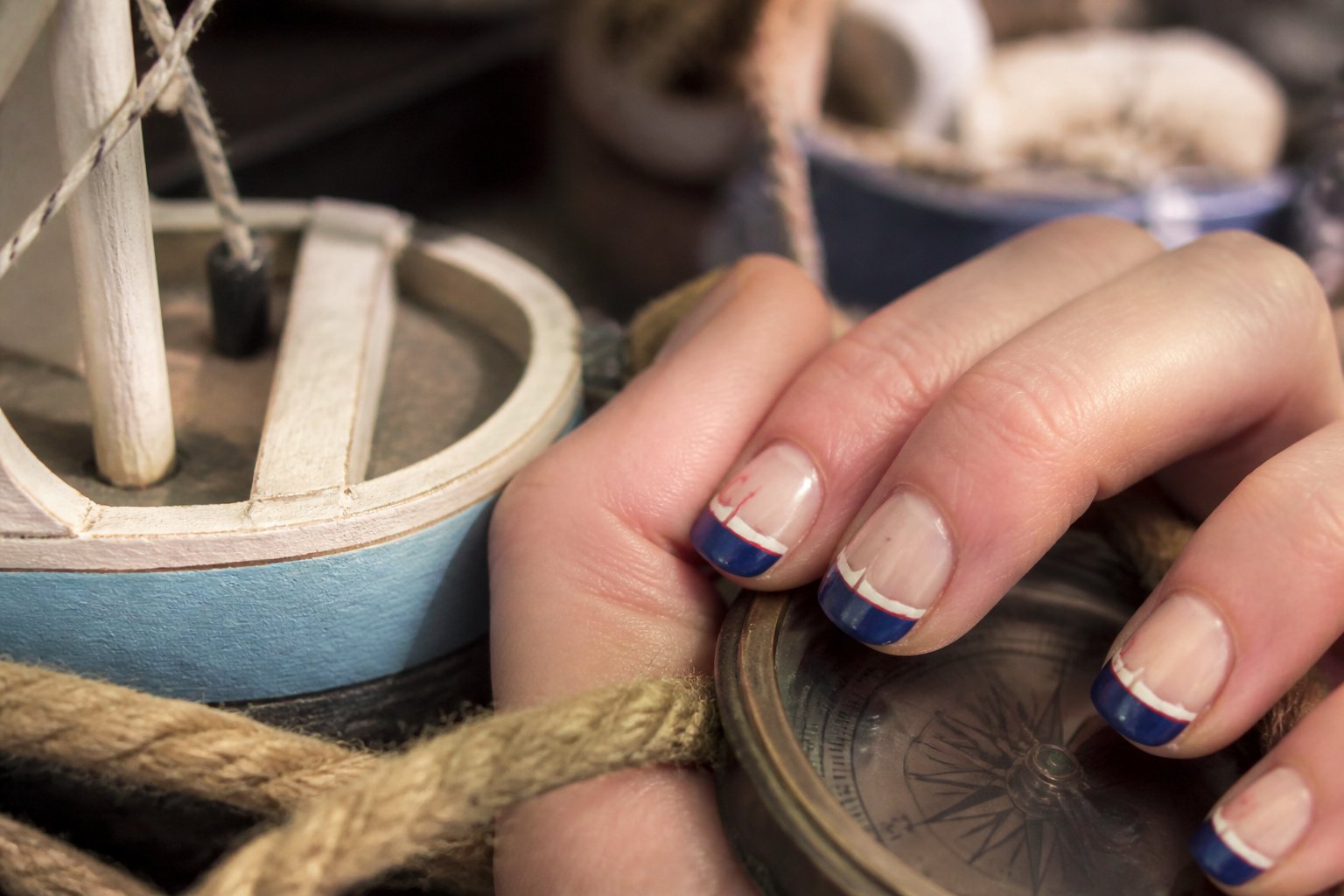 Close-up of hands with nautical-themed nails featuring sailor hat designs, surrounded by small nautical objects like rope and a wooden boat model.