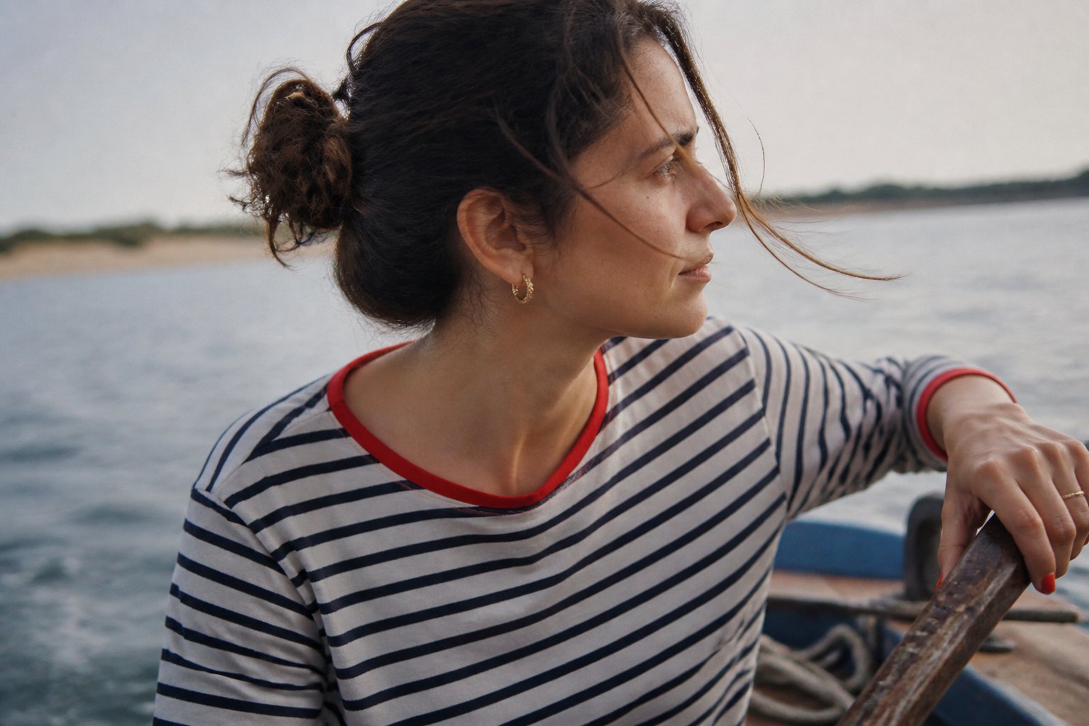 A woman wearing a striped Breton top with red trim in a casual indoor setting with natural light and soft shadows.