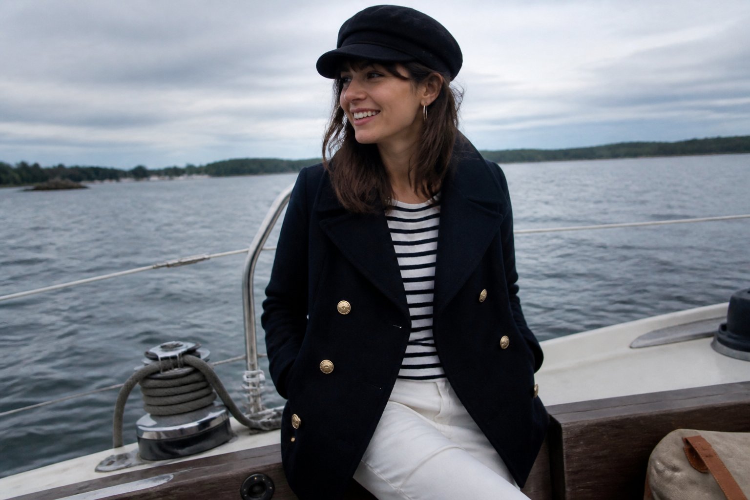 A woman wearing a navy double-breasted peacoat in a casual nautical outfit, standing in soft natural daylight with visible textures and slightly uneven shadows.