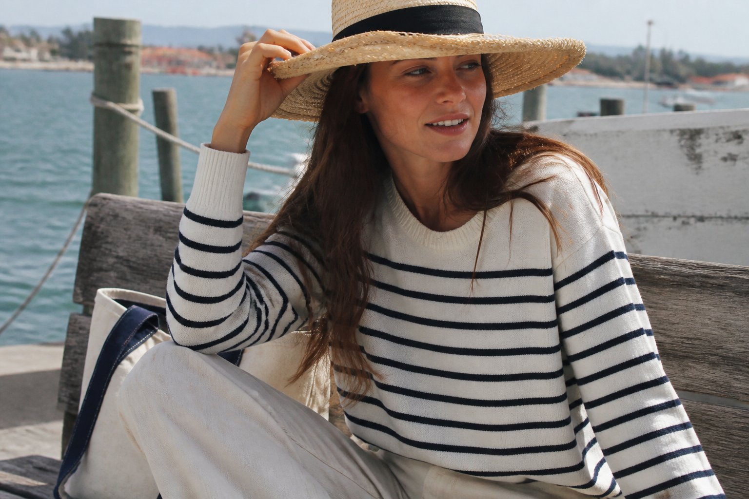 A woman wearing a wide-brim straw sun hat and nautical outfit outdoors with soft daylight and casual surroundings.