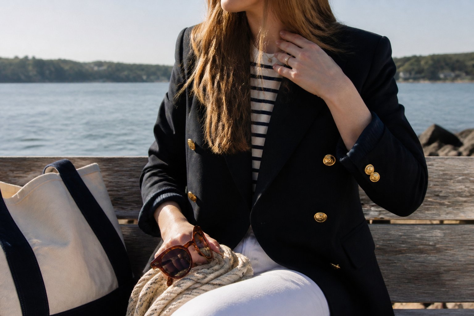 A woman wearing a classic navy blazer with gold buttons in a casual nautical outfit, standing outdoors with soft daylight and natural shadows.