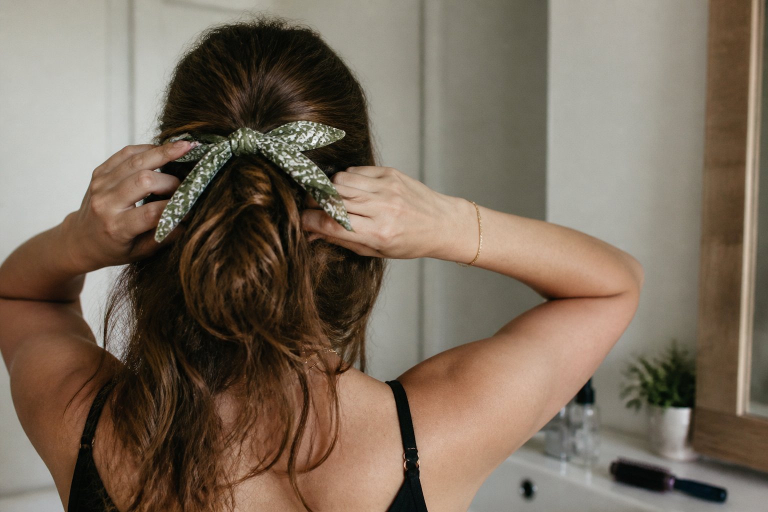 A person with a half-up twisted hairstyle secured by a folded bandana, shown in soft daylight with natural shadows and casual framing.