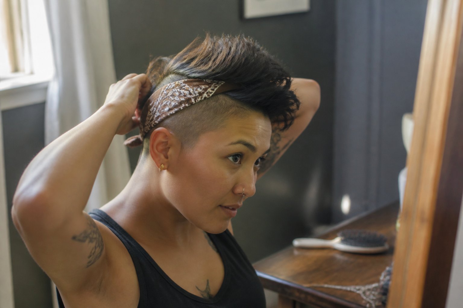 Person with a faux hawk hairstyle and bandana-wrapped sides in a softly lit casual setting with natural daylight.