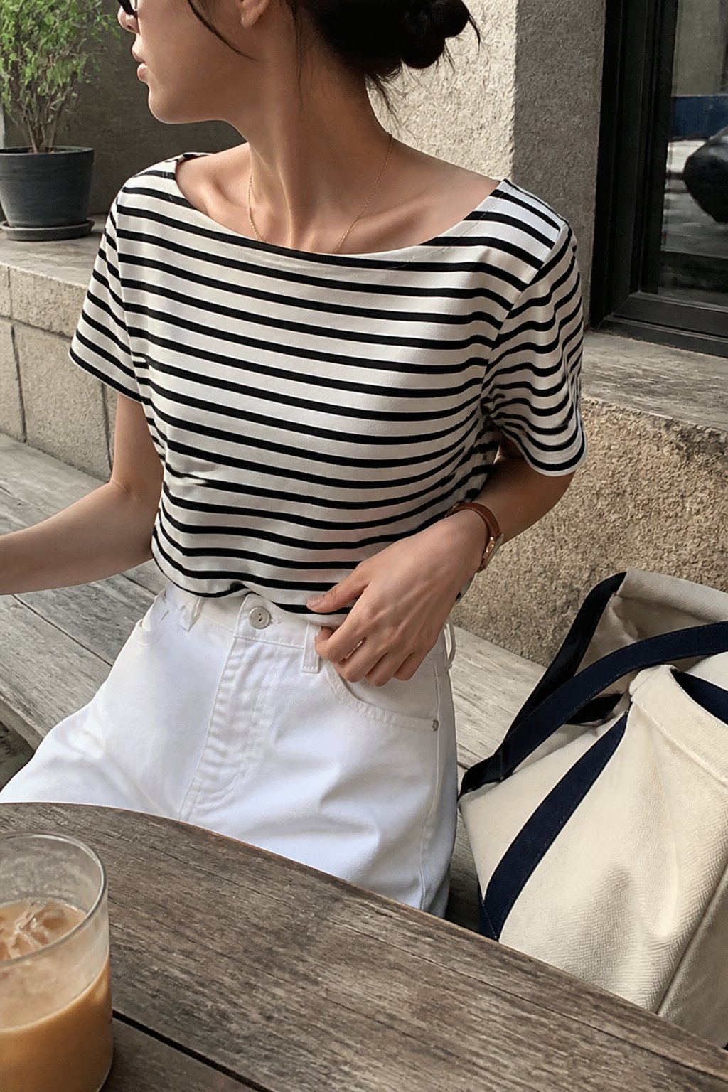 Person wearing a striped boatneck tee in a casual setting with natural daylight and everyday objects nearby.
