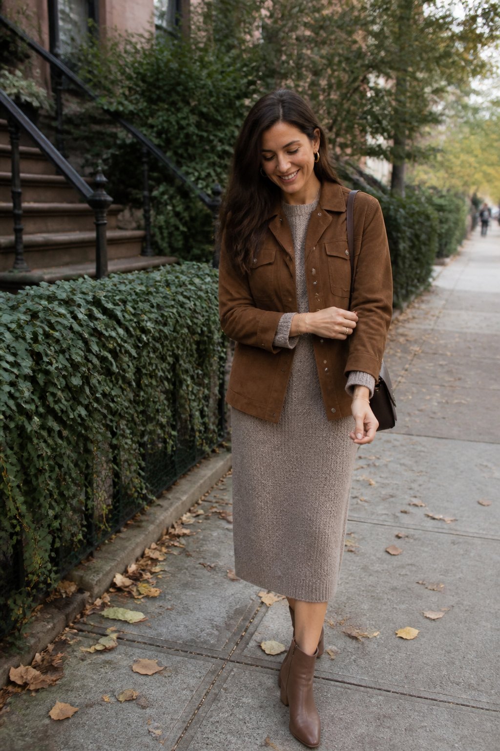 A woman wears a brown suede jacket over a knit dress with ankle boots in an autumn setting.