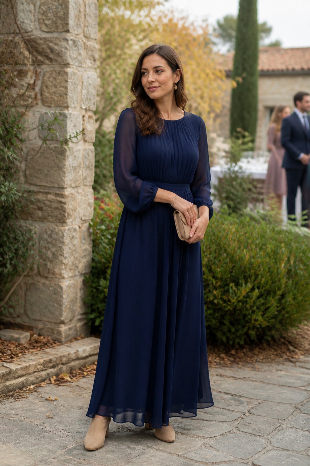 A woman wearing a navy long-sleeve chiffon maxi dress stands at an outdoor fall wedding venue.