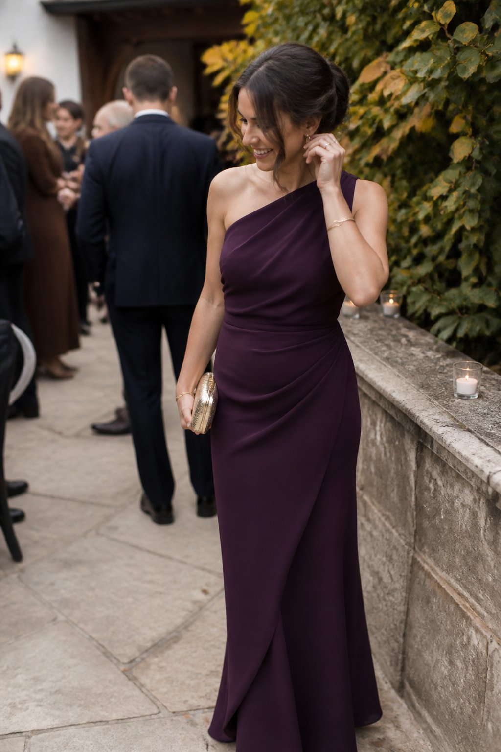 A woman wearing a plum one-shoulder dress stands at an autumn wedding venue.