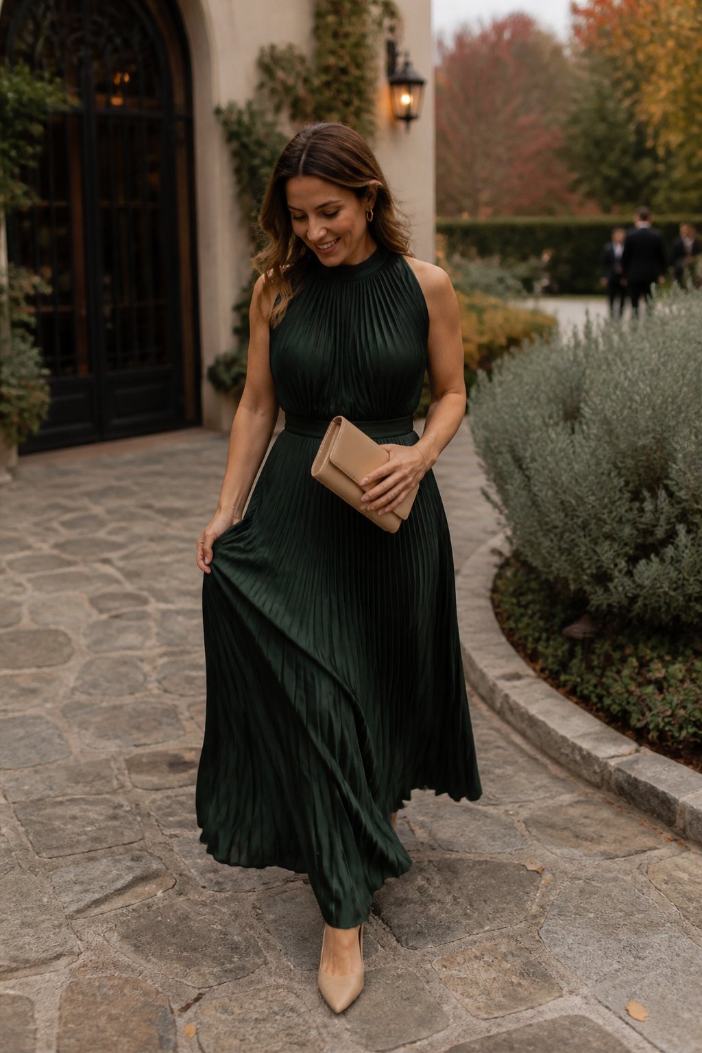 Woman wearing a forest green pleated maxi dress at an outdoor fall wedding venue.