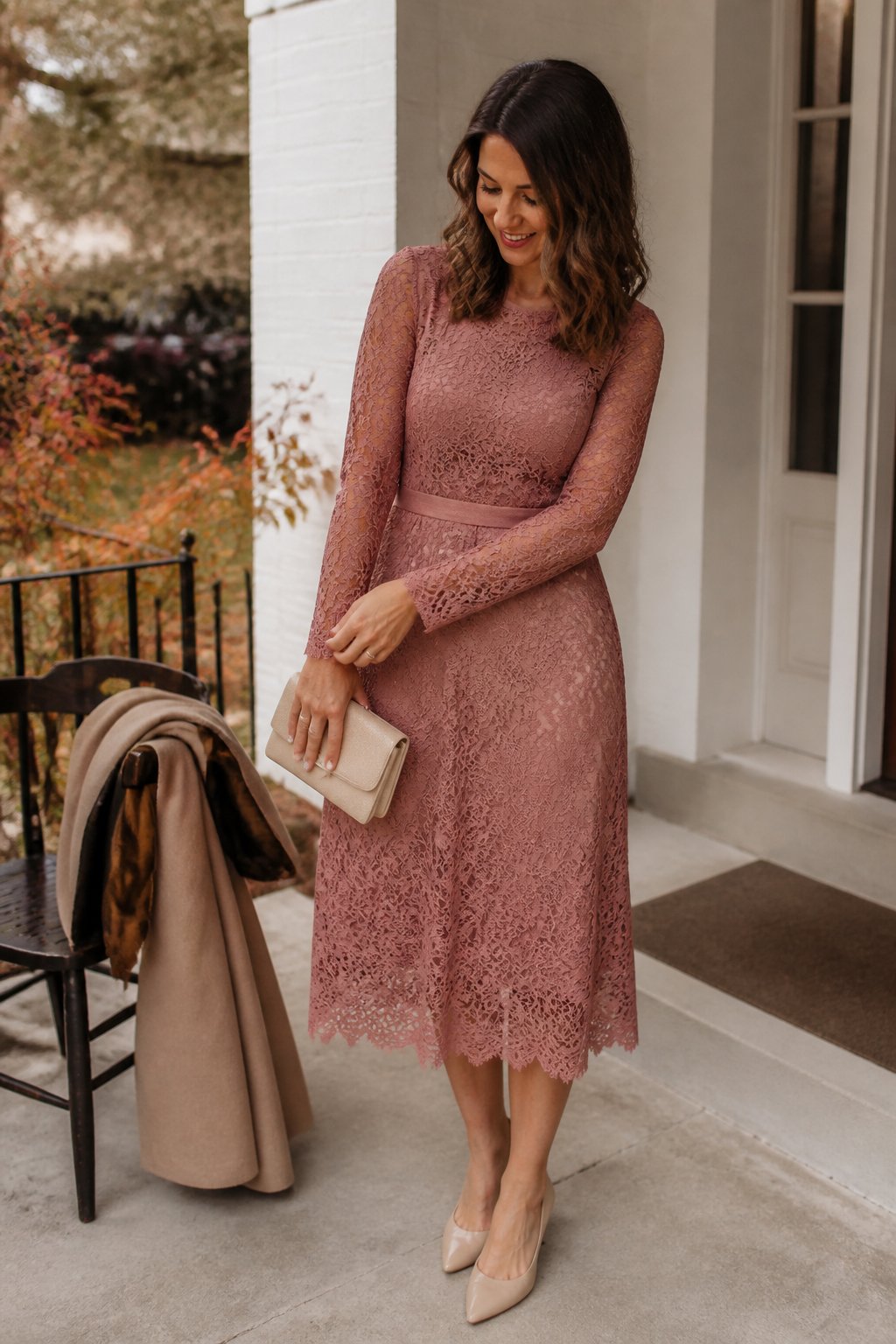 A woman wearing a dusty rose long-sleeve lace midi dress stands in a softly lit autumn setting.