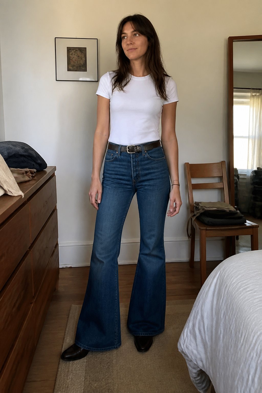 A person wears a fitted white T-shirt tucked into bell-bottom jeans with a leather belt.