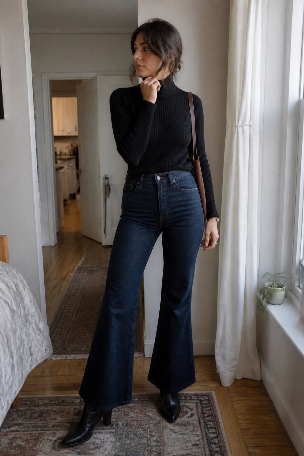A woman wears a fitted black turtleneck, dark bell-bottom jeans, and knee-high boots in a softly lit room.