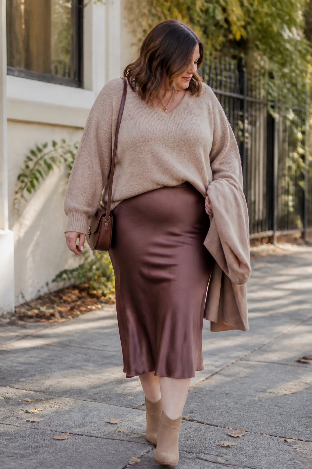 A midsize woman wears a chunky knit sweater with a satin midi skirt in a casual autumn setting.