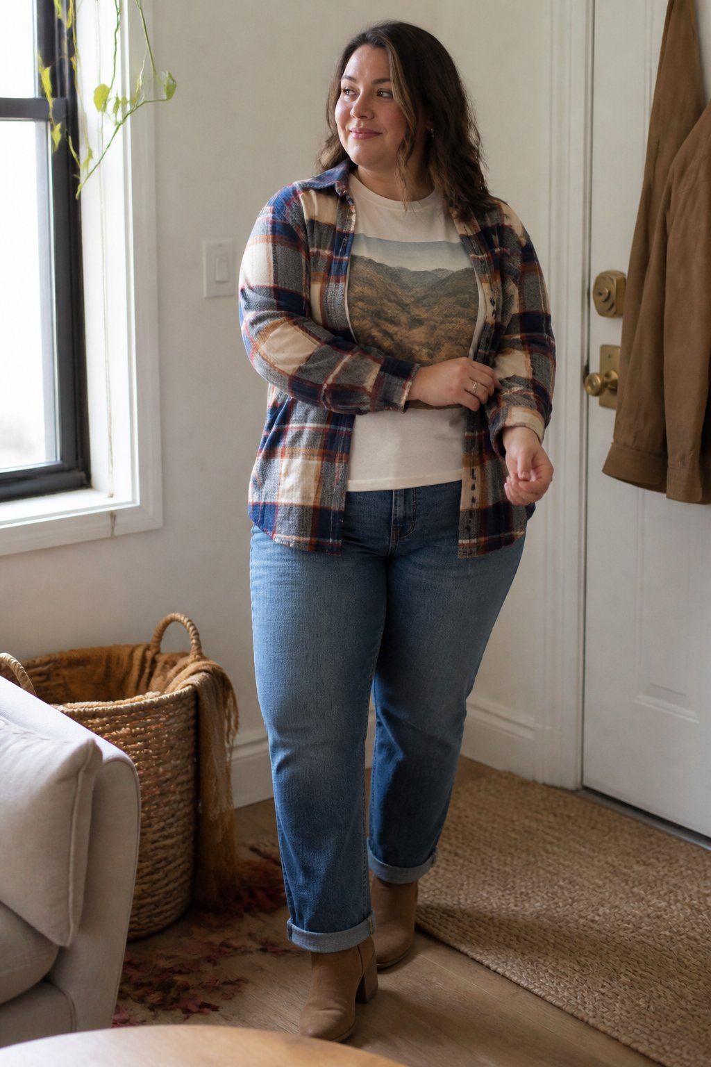 A woman with a fuller figure wears an open plaid flannel shirt over a graphic T-shirt and straight-leg jeans in a cozy home.