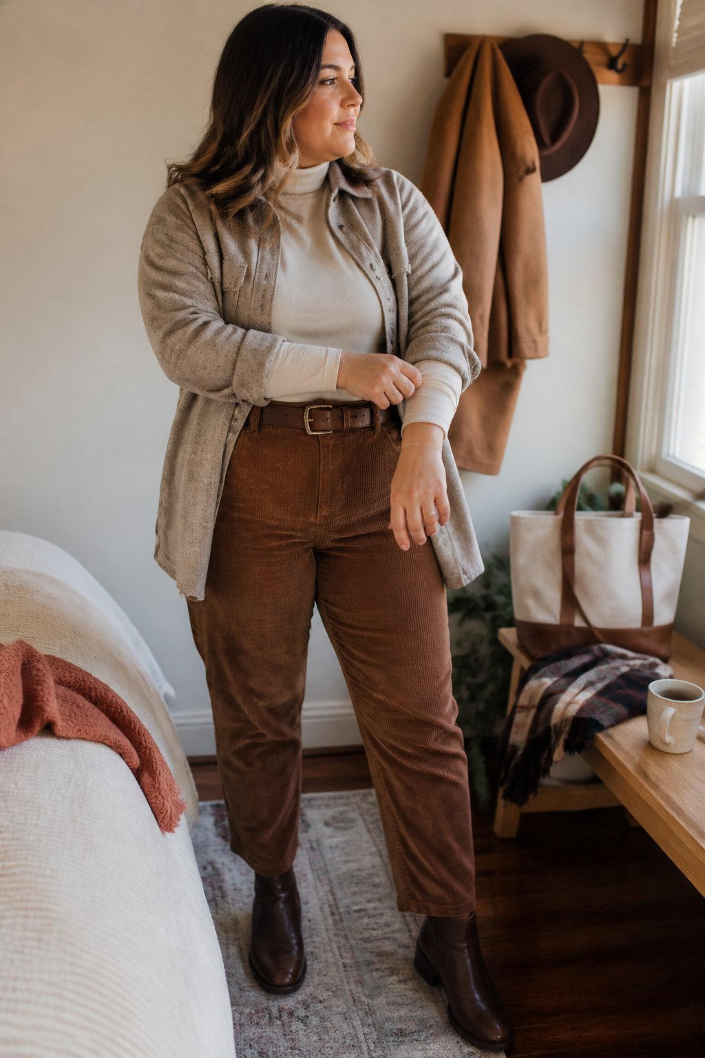 A midsize woman wearing brown corduroy pants and a light turtleneck stands in a warmly lit autumn interior.