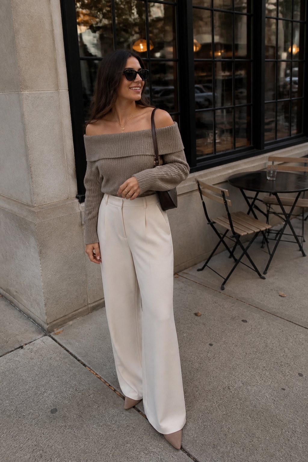 A woman wearing an off-the-shoulder knit top and wide-leg pants stands outside in a casual fall setting.