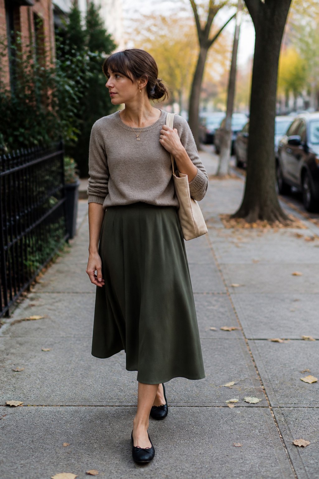 Woman wearing a midi skirt, fine-gauge sweater, and ballet flats on a leafy early autumn street.