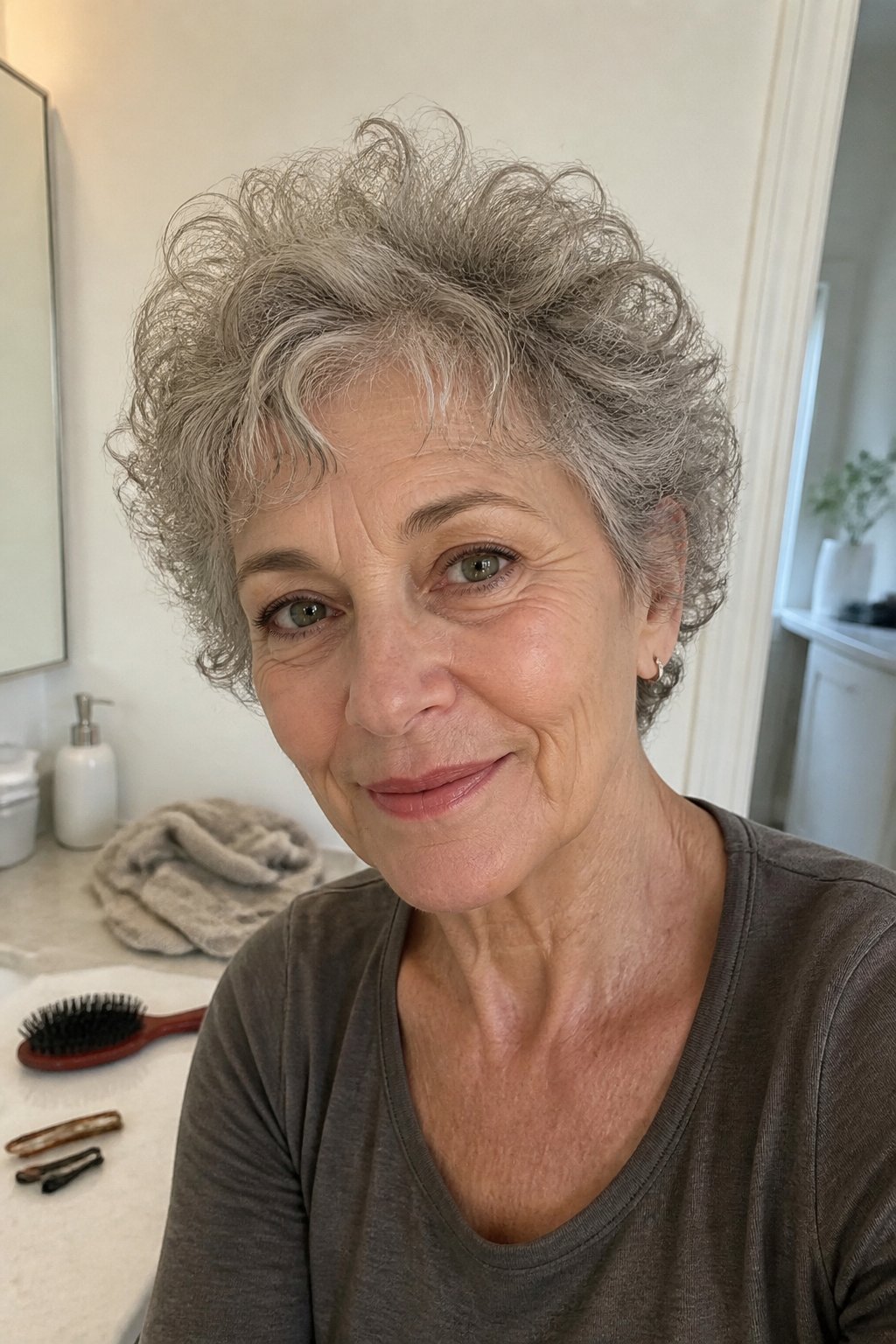An older woman with a short curly pixie haircut and wispy bangs stands in a softly lit home.