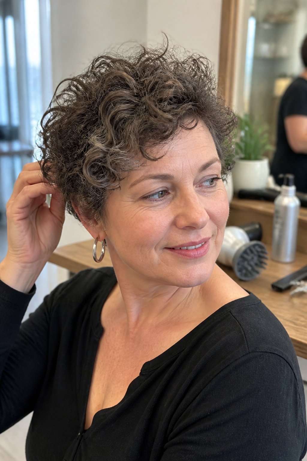 A woman with short, rounded curly pixie hair sits in a softly lit salon.
