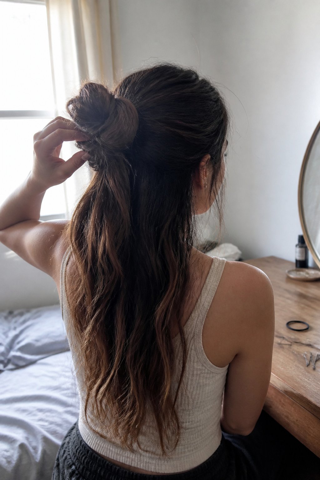 A person with long hair wears a relaxed half-up twisted bun while getting ready.