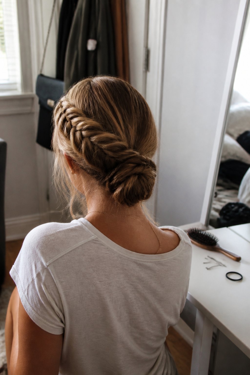 A person is shown from behind wearing a fishtail braid coiled into a low updo.