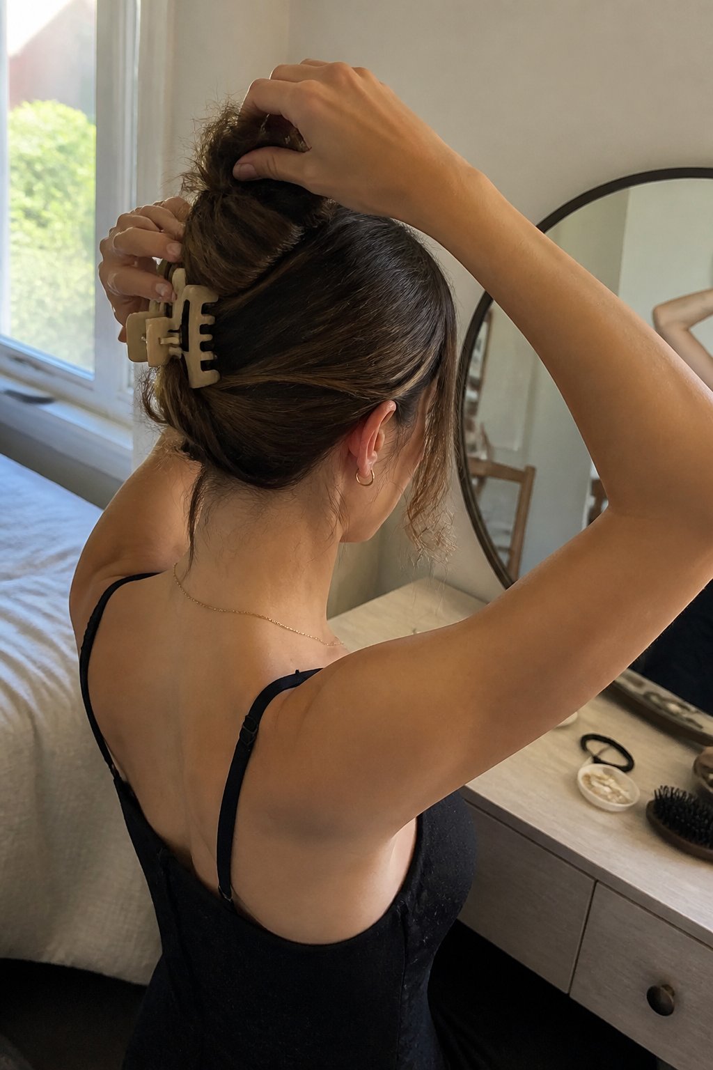 A person with medium-length hair secures a French twist with a claw clip while getting ready.