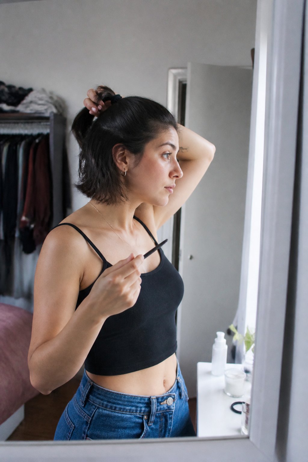 A person with short hair gathers the top section into a small half-up ponytail while getting ready for a concert.